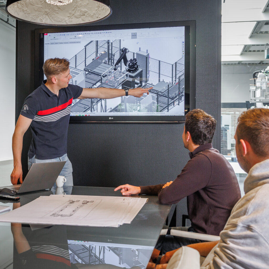 Sismatec-engineer presenteert een 3D-ontwerp van een geautomatiseerde verpakkingslijn aan collega’s.