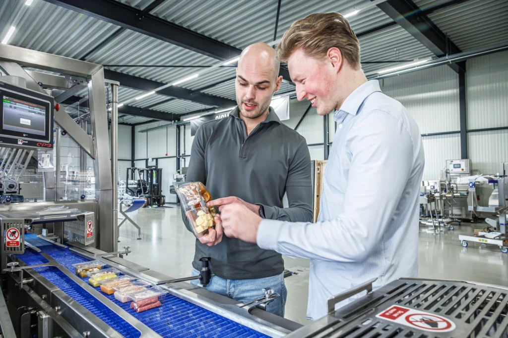 Twee medewerkers controleren verpakte voedingsproducten bij een geautomatiseerde Proseal-verpakkingslijn.