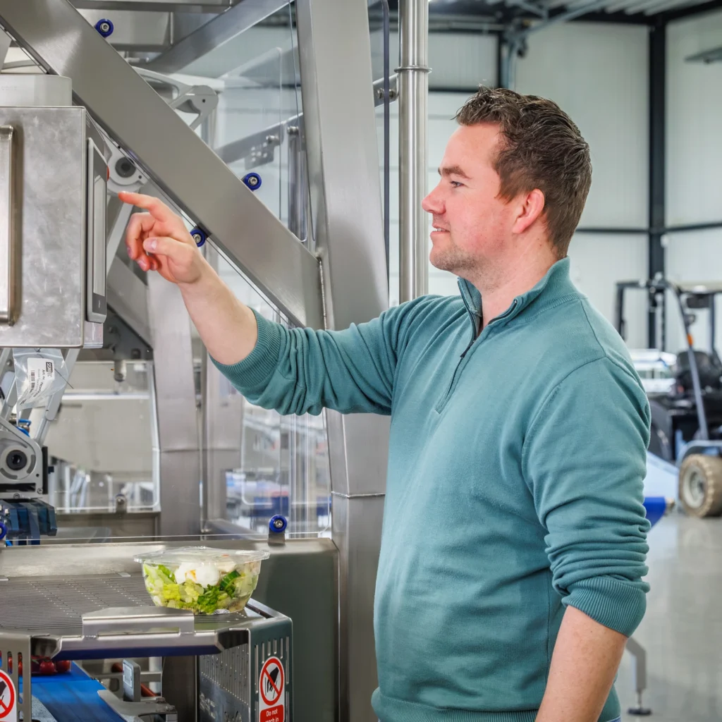 Sismatec-medewerker bedient een verpakkingsmachine voor het automatisch verpakken van maaltijdsalades.