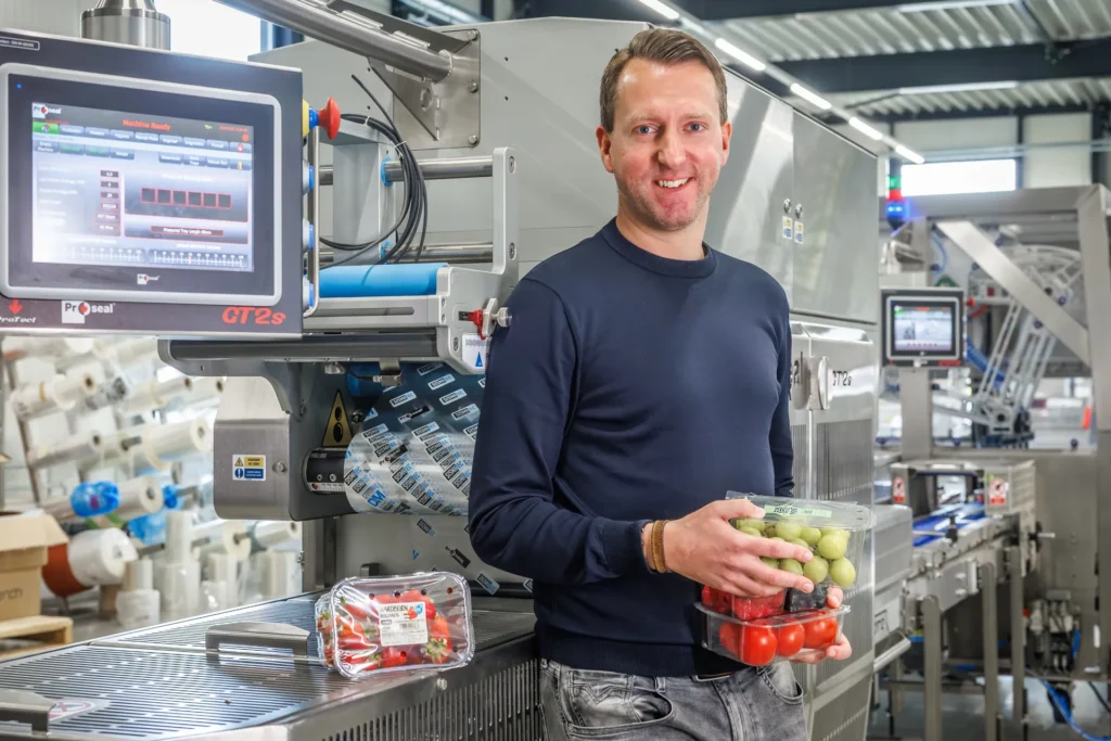 Sismatec-medewerker toont verpakte druiven, aardbeien en tomaten bij een Proseal-traysealer voor de AGF-industrie.