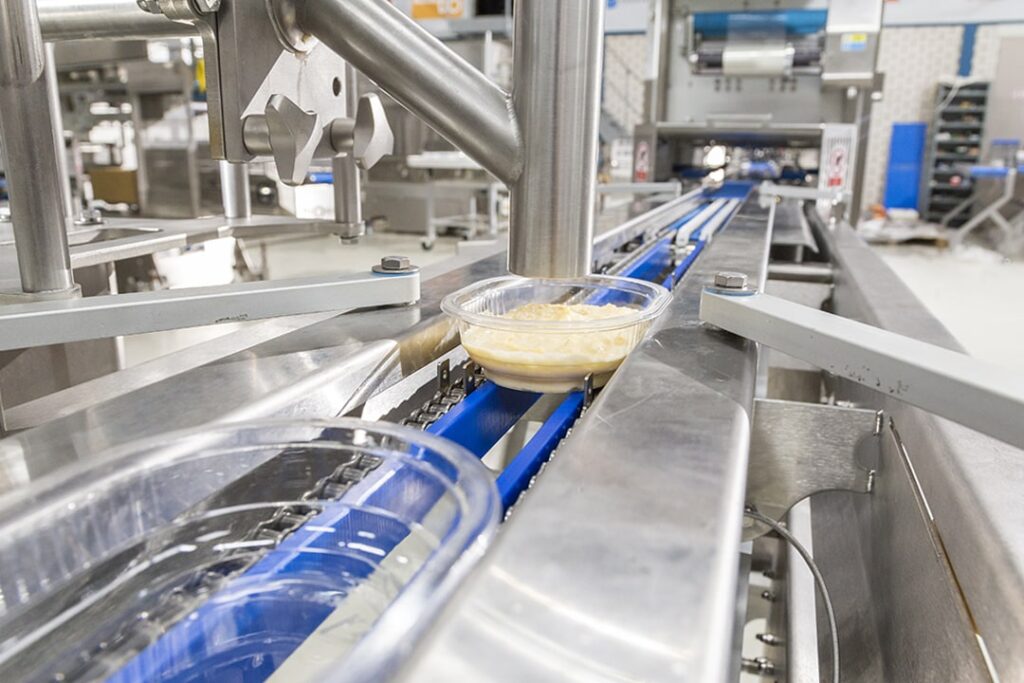 Schalen die gevuld worden met een vers voedingsproduct op een geautomatiseerde verpakkingslijn voor de voedingsindustrie.