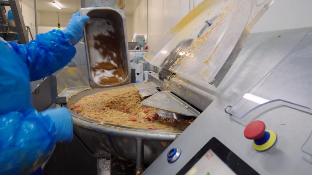 Medewerker voegt ingrediënten toe aan een industriële mengmachine voor de bereiding van voedingsmiddelen.