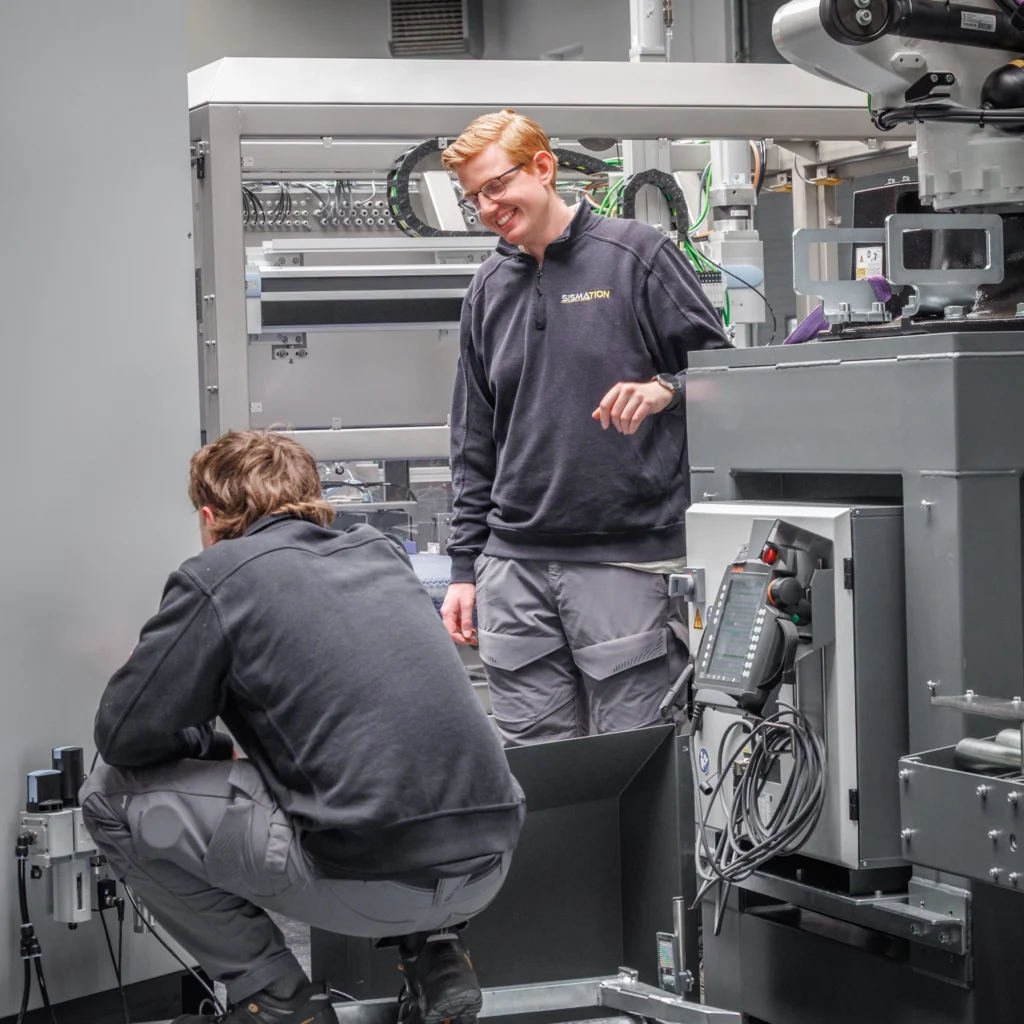 Twee Sismation-monteurs werken aan een automatiseringsmachine voor industriële verpakkingslijnen.