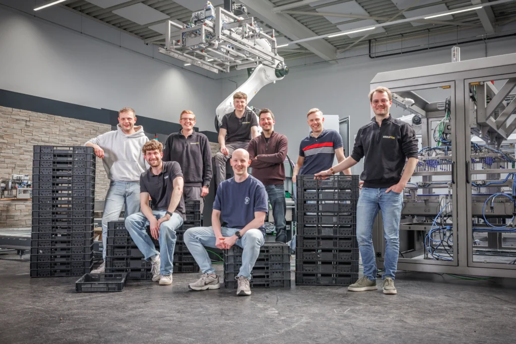 Het Sismation-team bij een robotgestuurde krattenopzetter voor het automatiseren van industriële verpakkingslijnen.