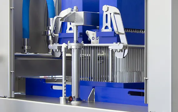 Detail van de naalden en producttransportband van een industriële pekelinjector voor het gelijkmatig injecteren van vleesproducten.